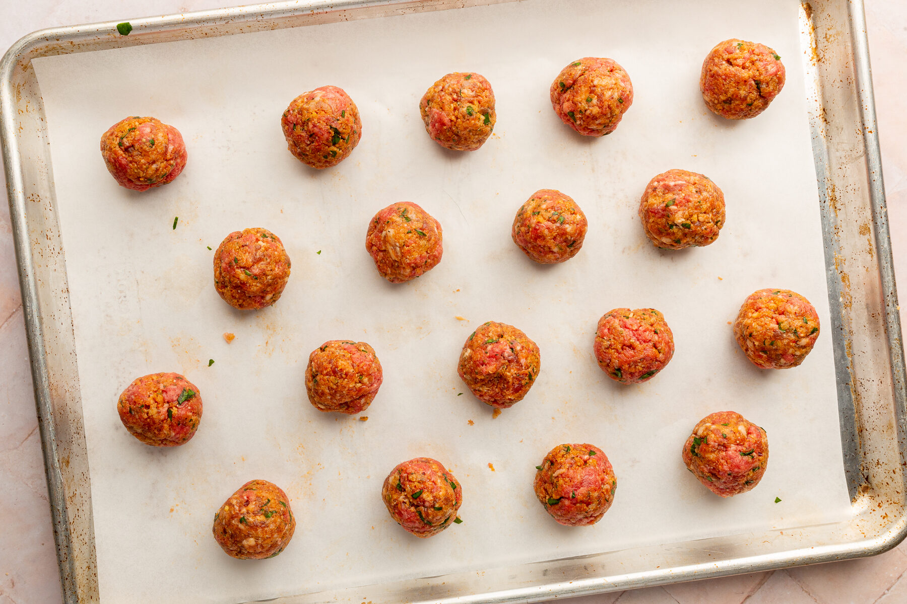 Spicy meatballs rolled into balls, spaced evenly, resting on parchment paper on a baking sheet.