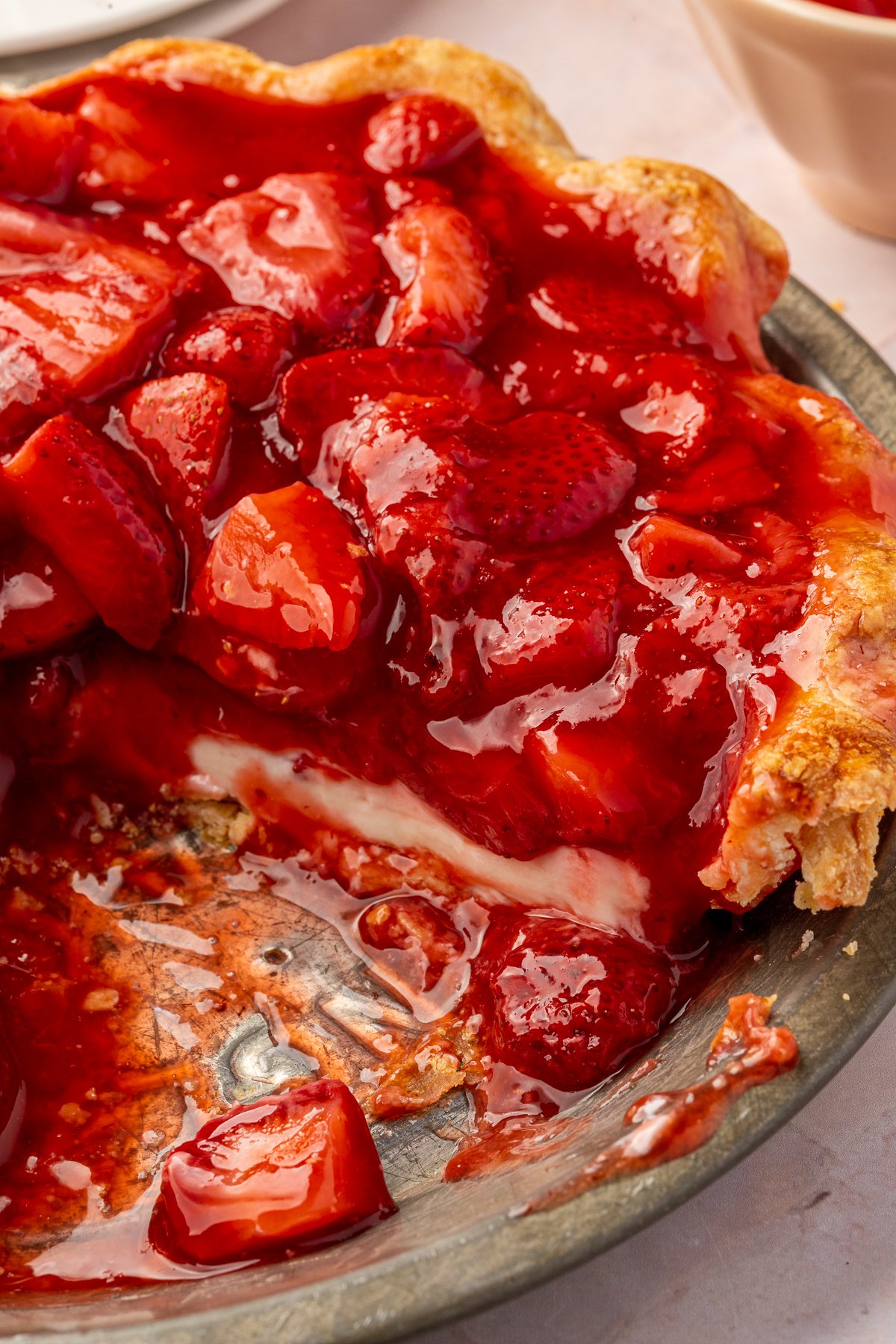 A close-up of the inside of the pie where a slice has been removed, showing the layers of creamy filling and strawberries in the flaky crust.