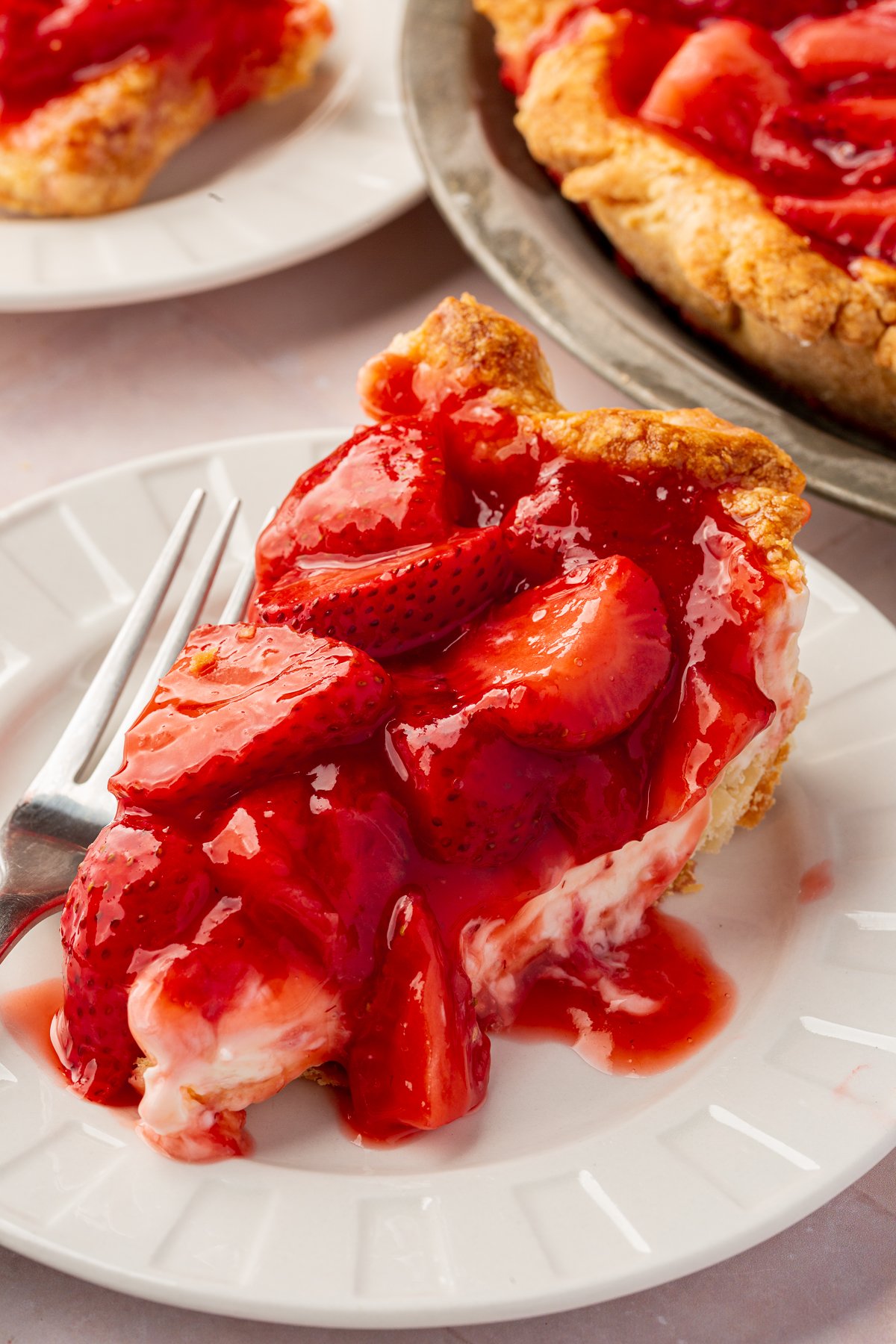 A slice of gluten-free strawberry cream cheese pie on a white plate, with bright red strawberries topping the smooth cream cheese layer and a fork resting beside it.