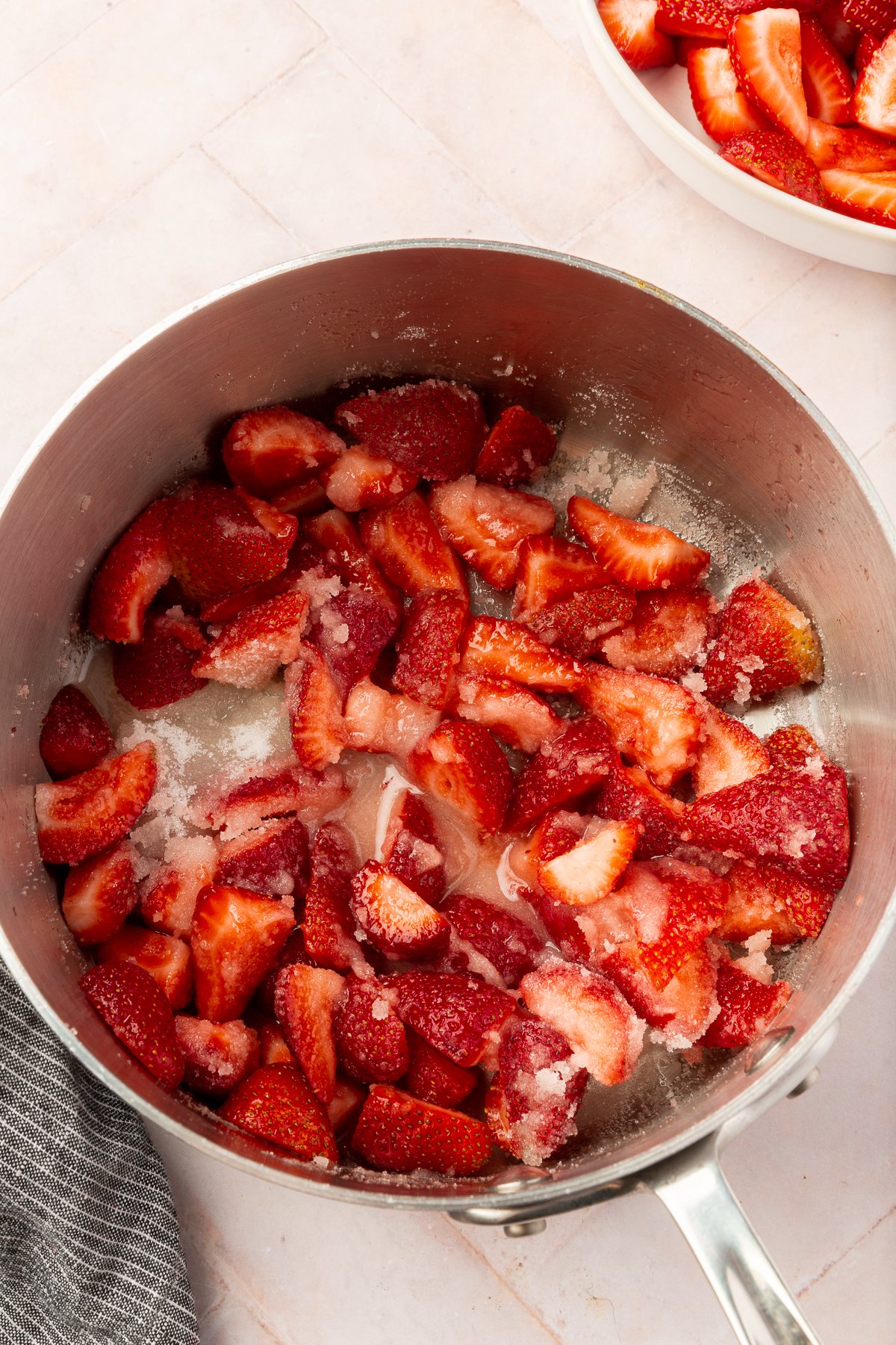 Freshly cut strawberries mixed with sugar in a saucepan, beginning to soften and release their juices.