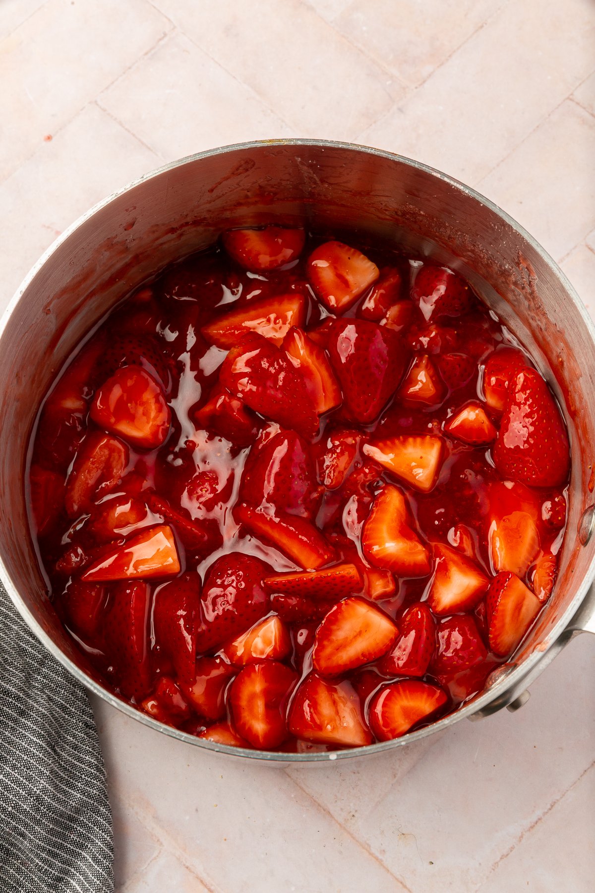 Fresh strawberries in a saucepan, simmering in their juices, with a glossy, thickening appearance.