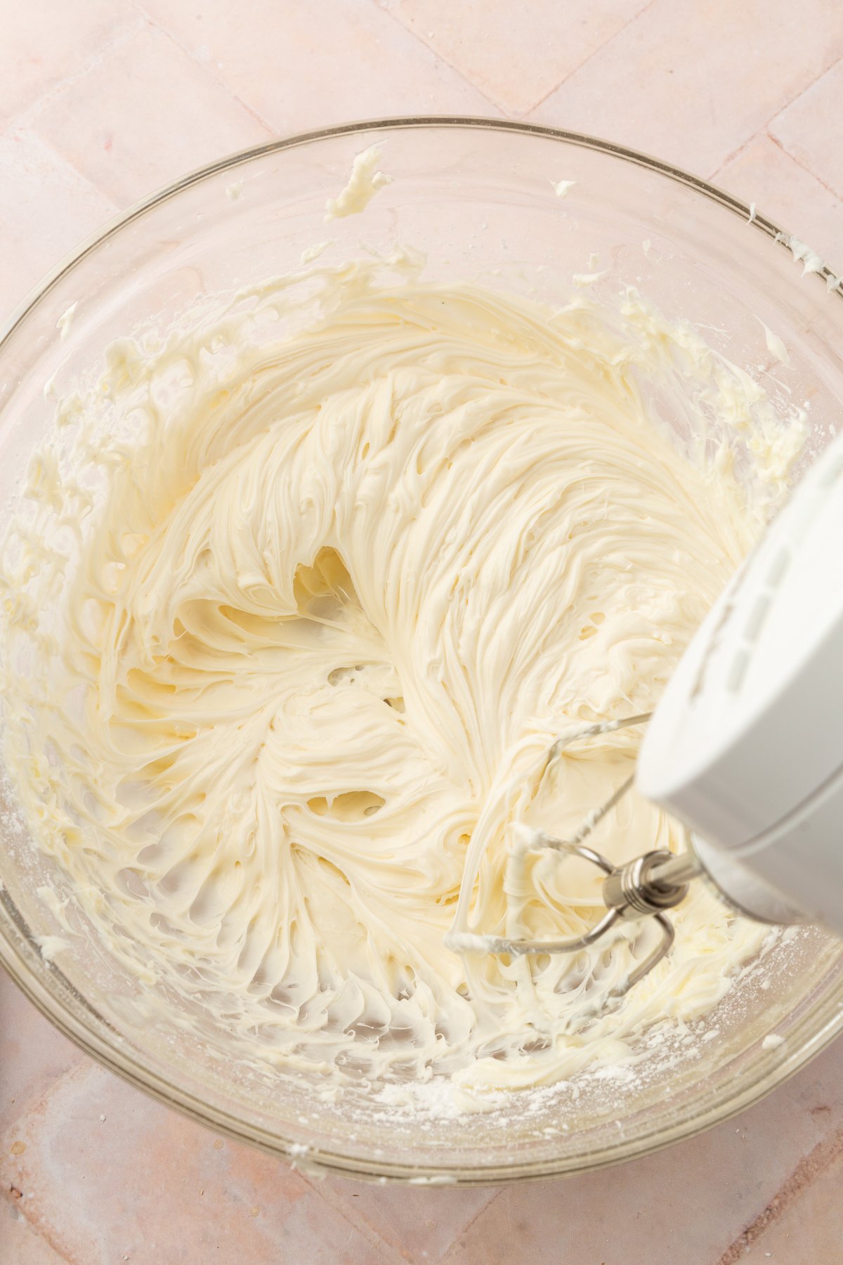 Smooth, creamy, whipped cream cheese filling in a glass bowl being mixed with an electric hand mixer.