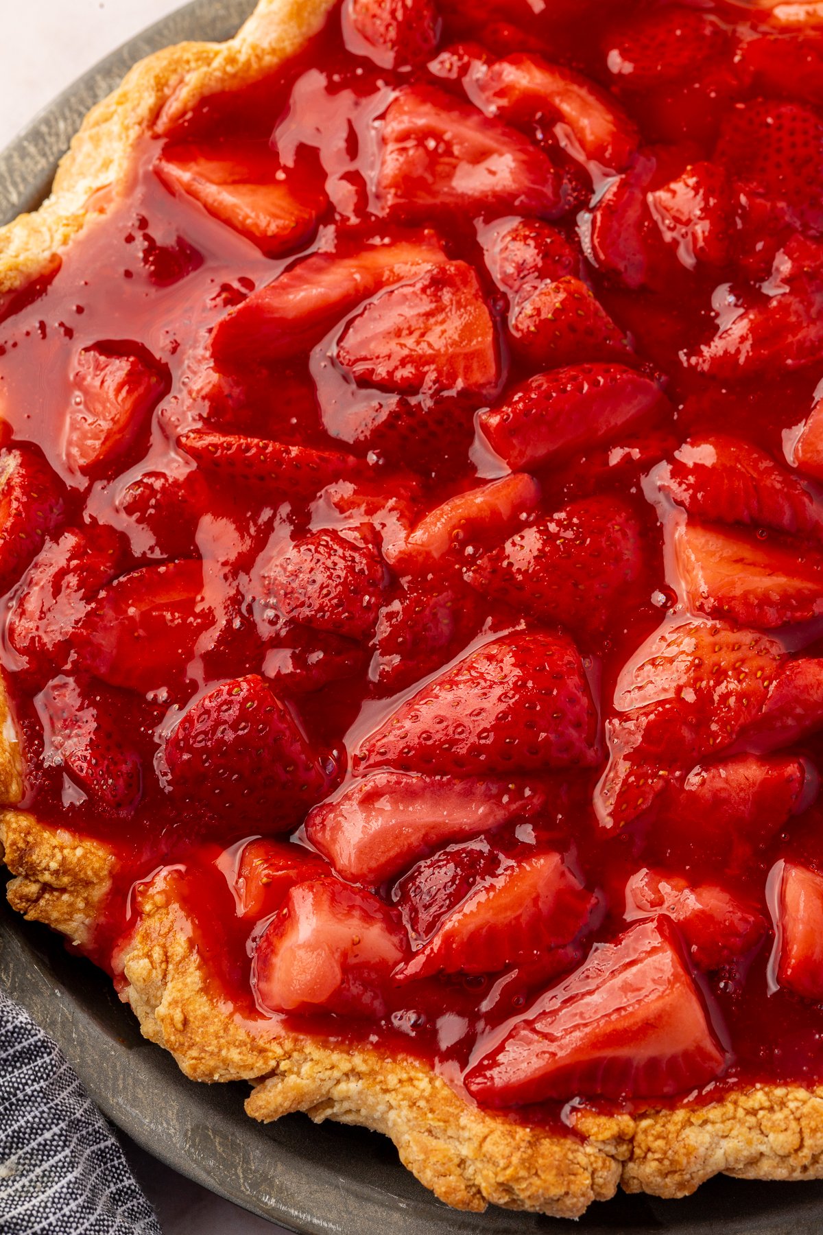 Bright red, glossy strawberry topping spread evenly over the cream cheese filling in the pie crust.