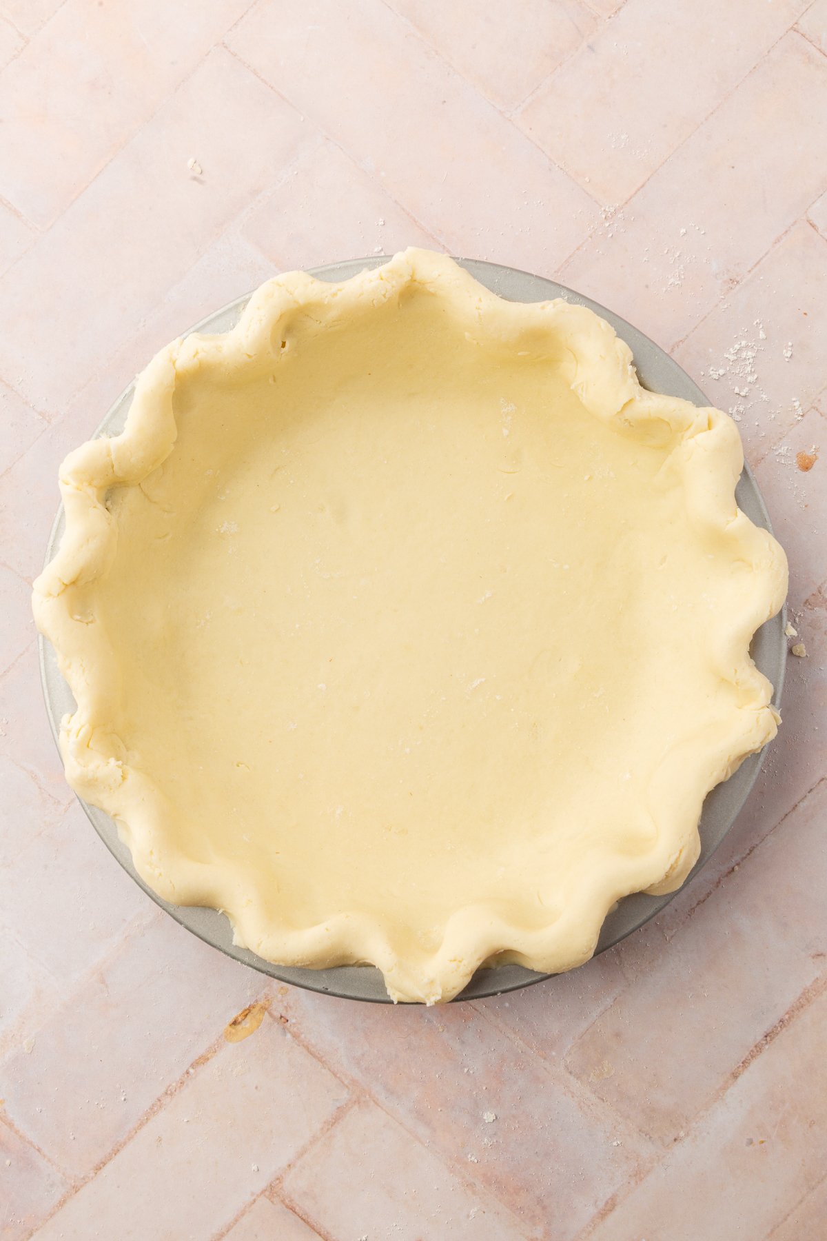 An unbaked pie crust neatly pressed into a pie pan with fluted edges on a light pink tiled surface
