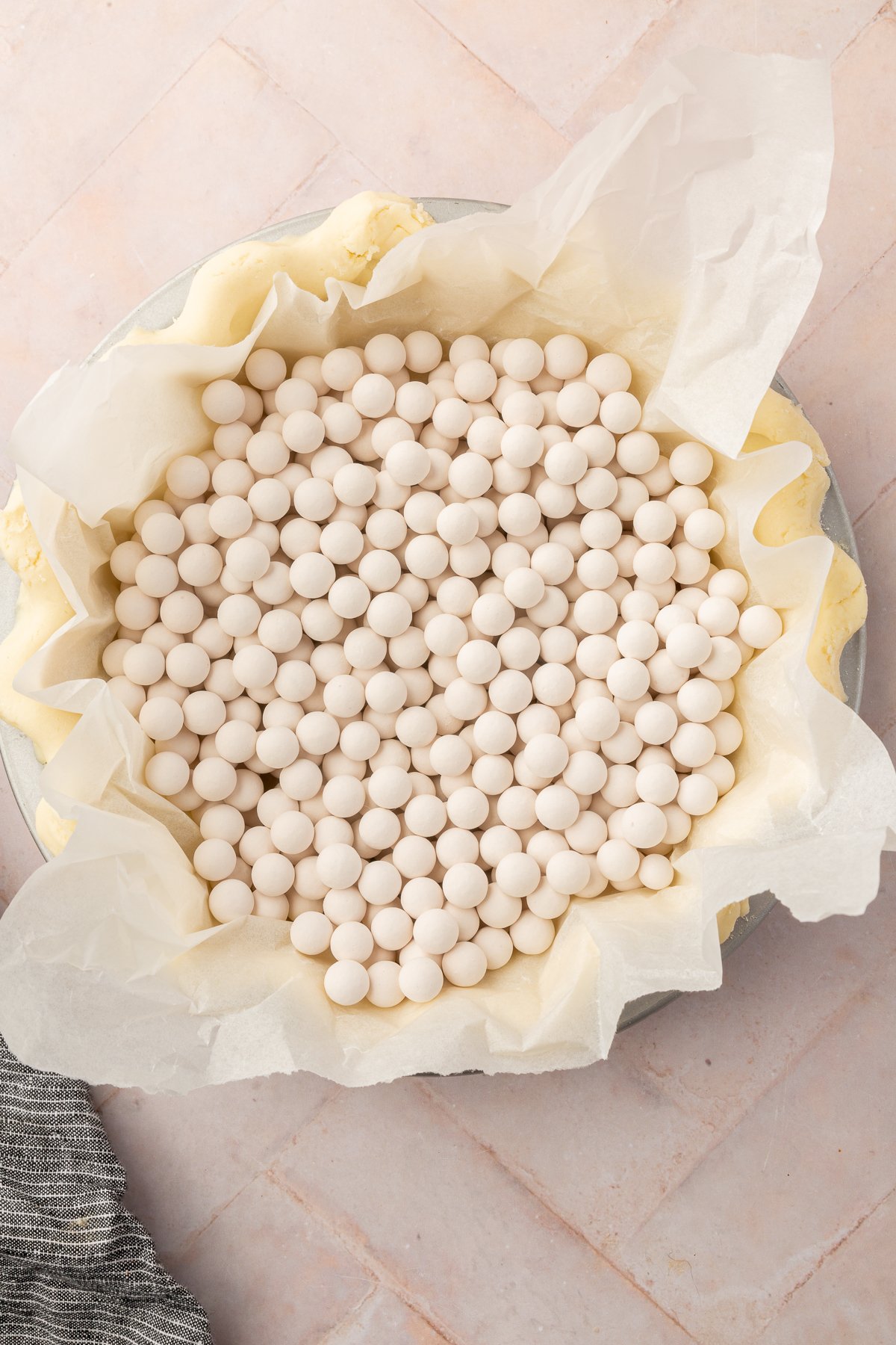 A parchment-lined pie crust filled with white ceramic pie weights, preparing the crust for blind baking.