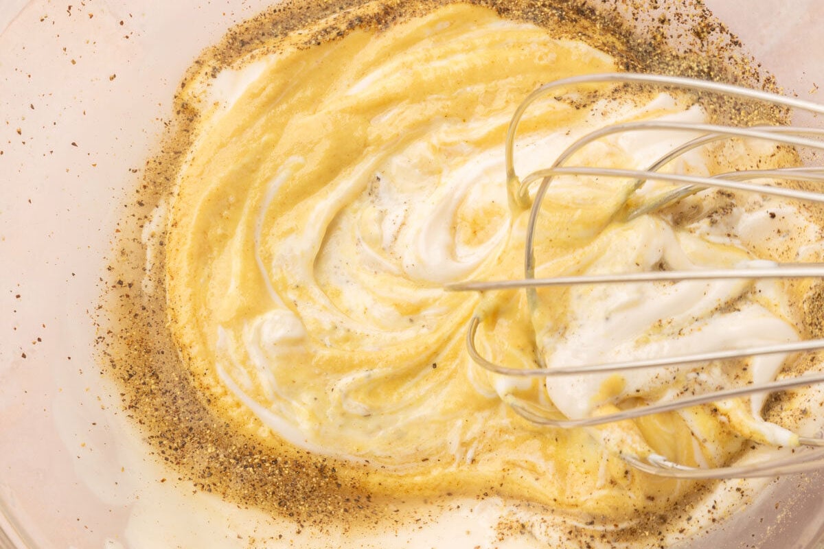 Mayonnaise, dijon mustard, lemon juice, salt and pepper being whisked together in a large mixing bowl.