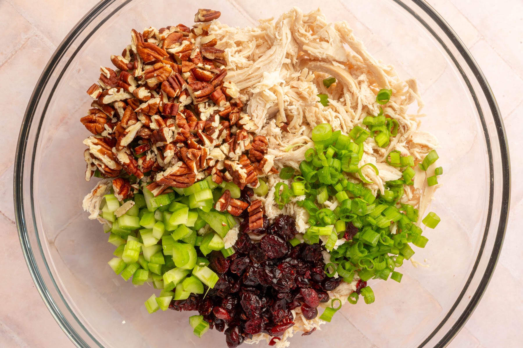 Cooked chicken celery, dried cranberries, celery, green onion and pecans in a mixing bowl before they are mixed together.