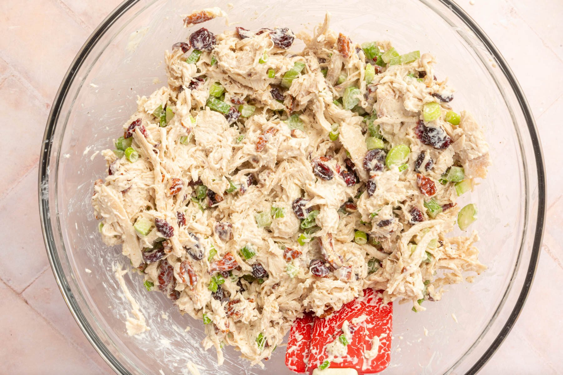 Cranberry pecan chicken salad being mixed in a large mixing bowl on a brick countertop