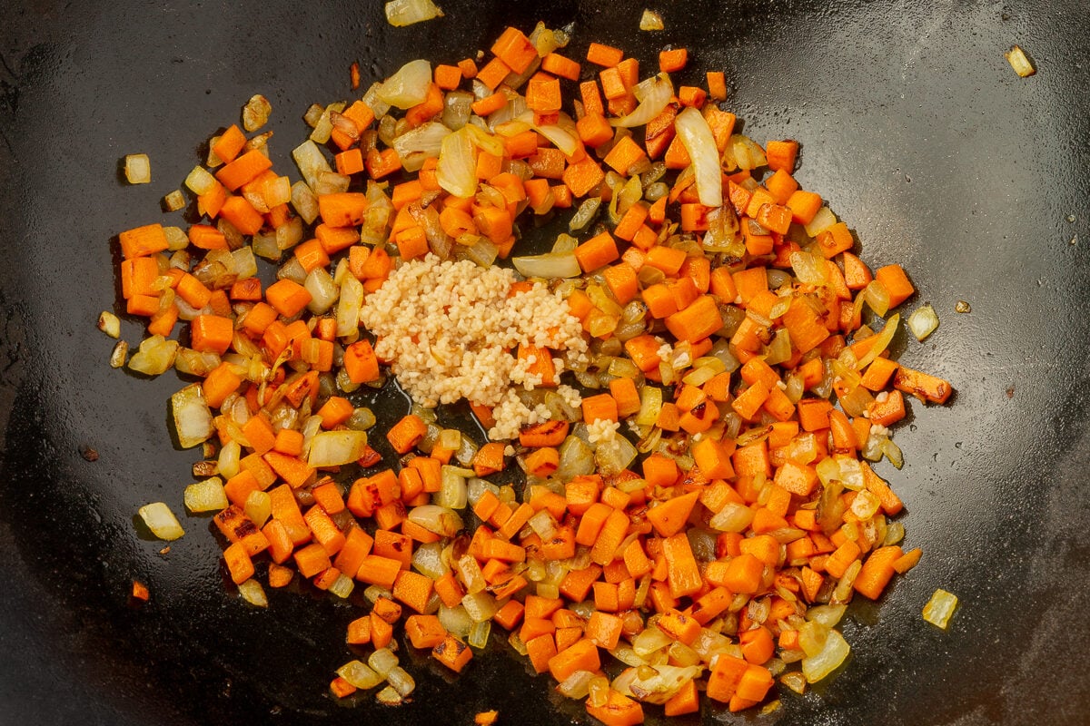 Further back image of carrots, onions and garlic in large wok.