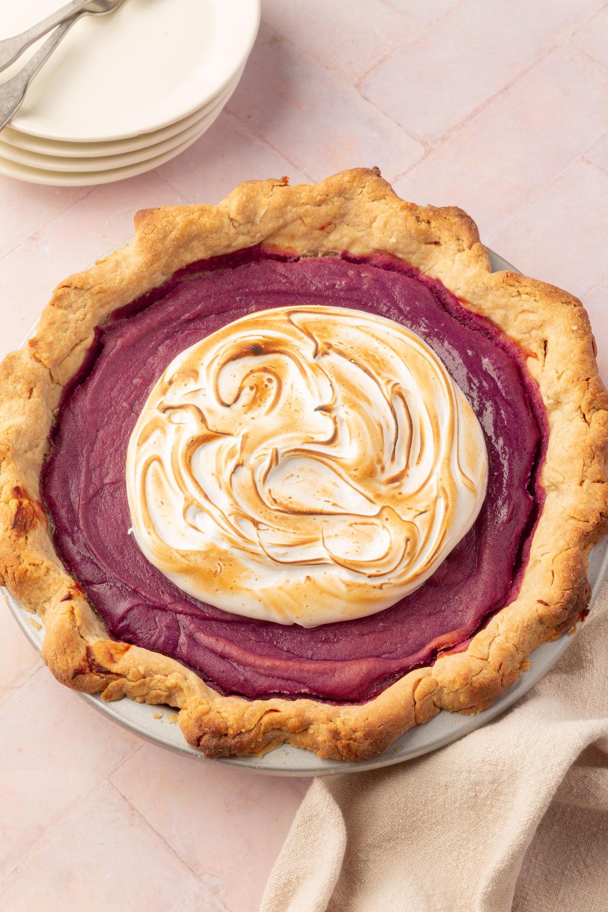 A close-up of a slice of purple sweet potato pie, focusing on the smooth purple filling, golden meringue, and flaky gluten-free crust.
