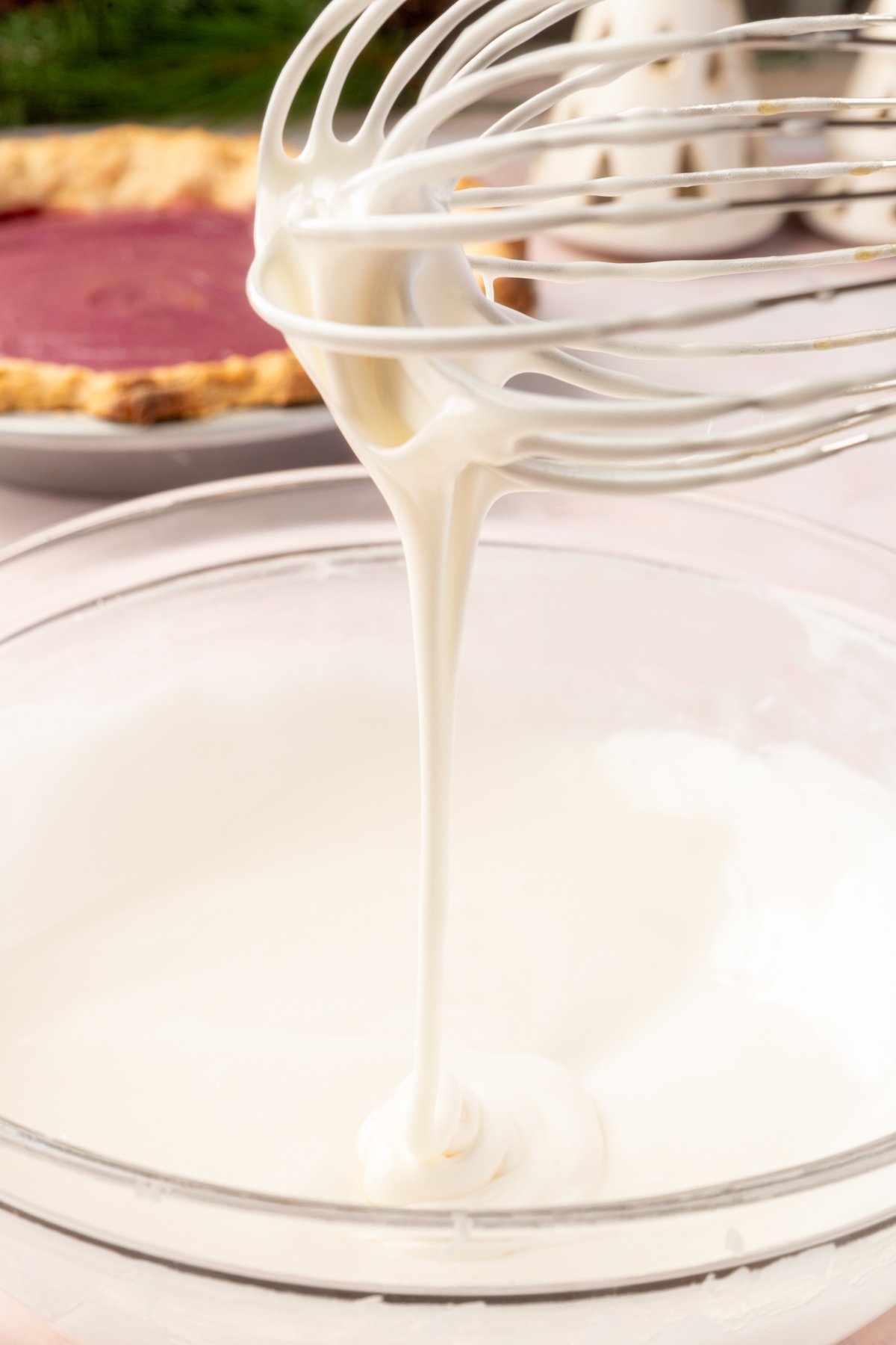 A whisk lifting a ribbon of glossy white marshmallow meringue, before whisking into stiff peaks.