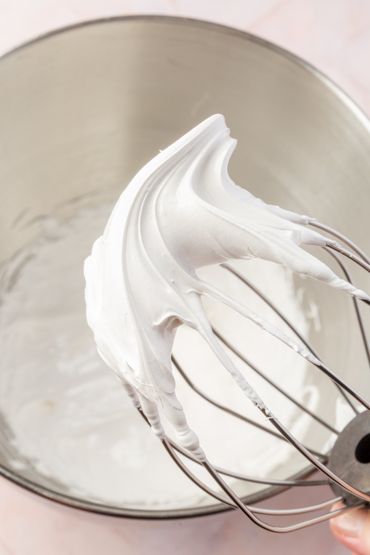 A close-up of a metal whisk with stiff marshmallow meringue peaks, highlighting the fluffy and smooth texture.