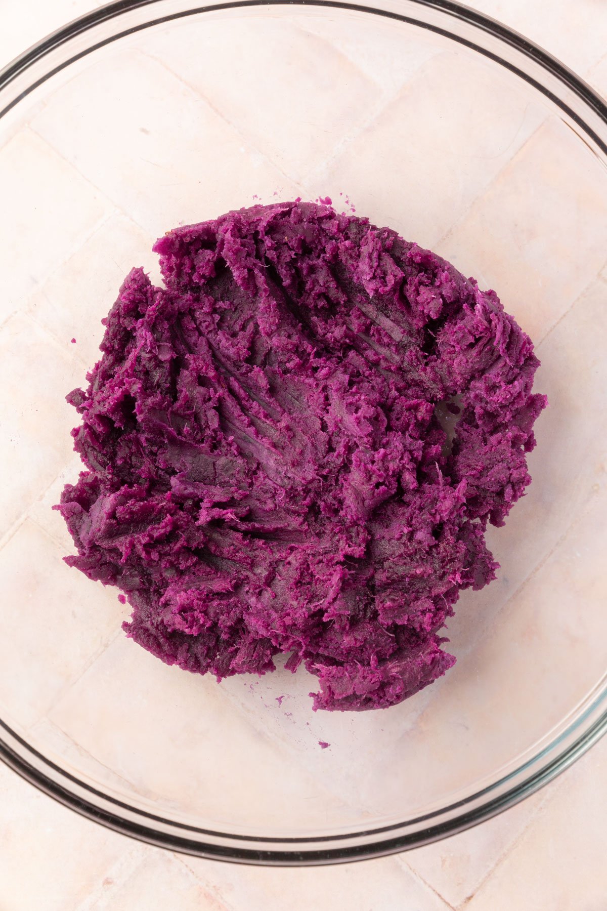 Mashed purple sweet potato in a clear glass bowl, showing the vibrant purple color and smooth texture.