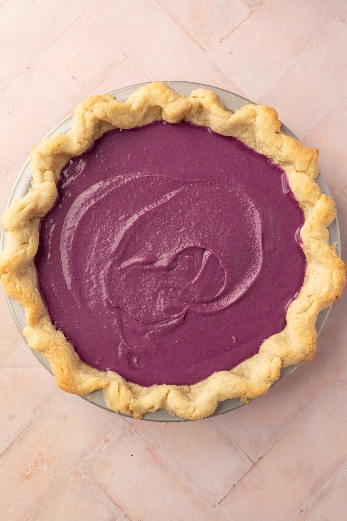 The purple sweet potato pie filling spread evenly inside the gluten-free pie crust, ready for baking.
