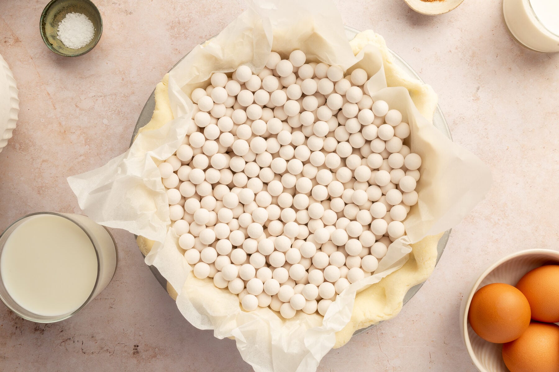 Image of uncooked gluten-free pie crust set in a pie dish, with parchment paper and pie weights resting in the pie dish