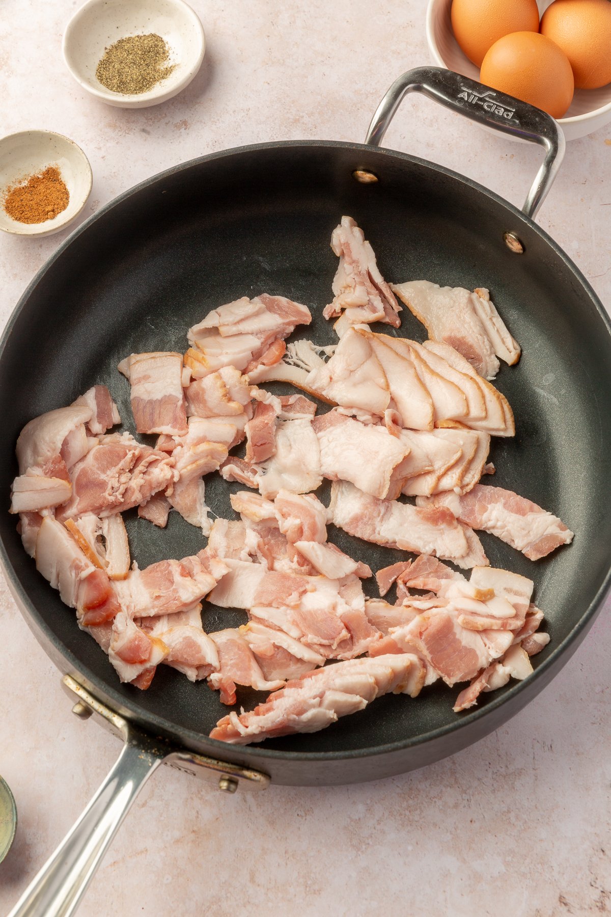 Uncooked bacon in a large skilled on a marble countertop.