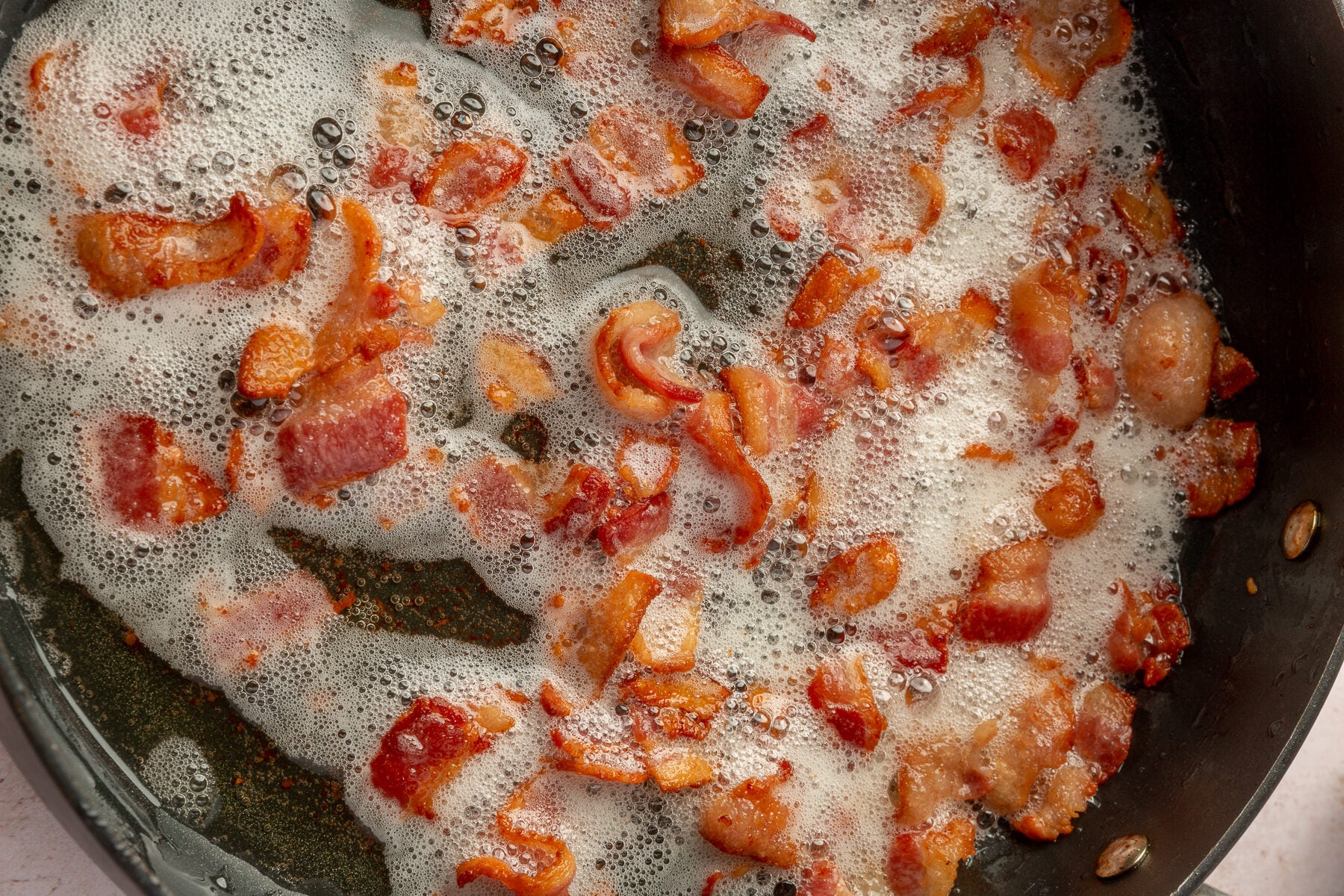 Close up image of bacon cooking in a large skillet.
