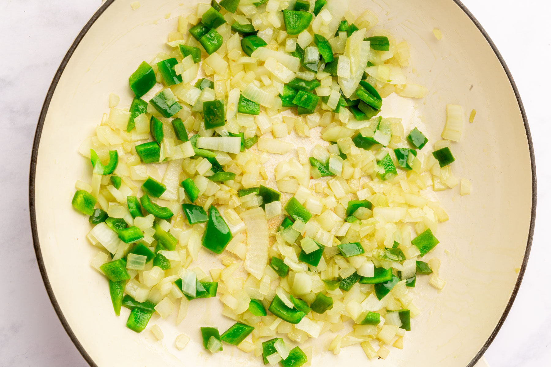 Large mixing bowl with minced garlic, green bell pepper and yellow onion mixed in it.