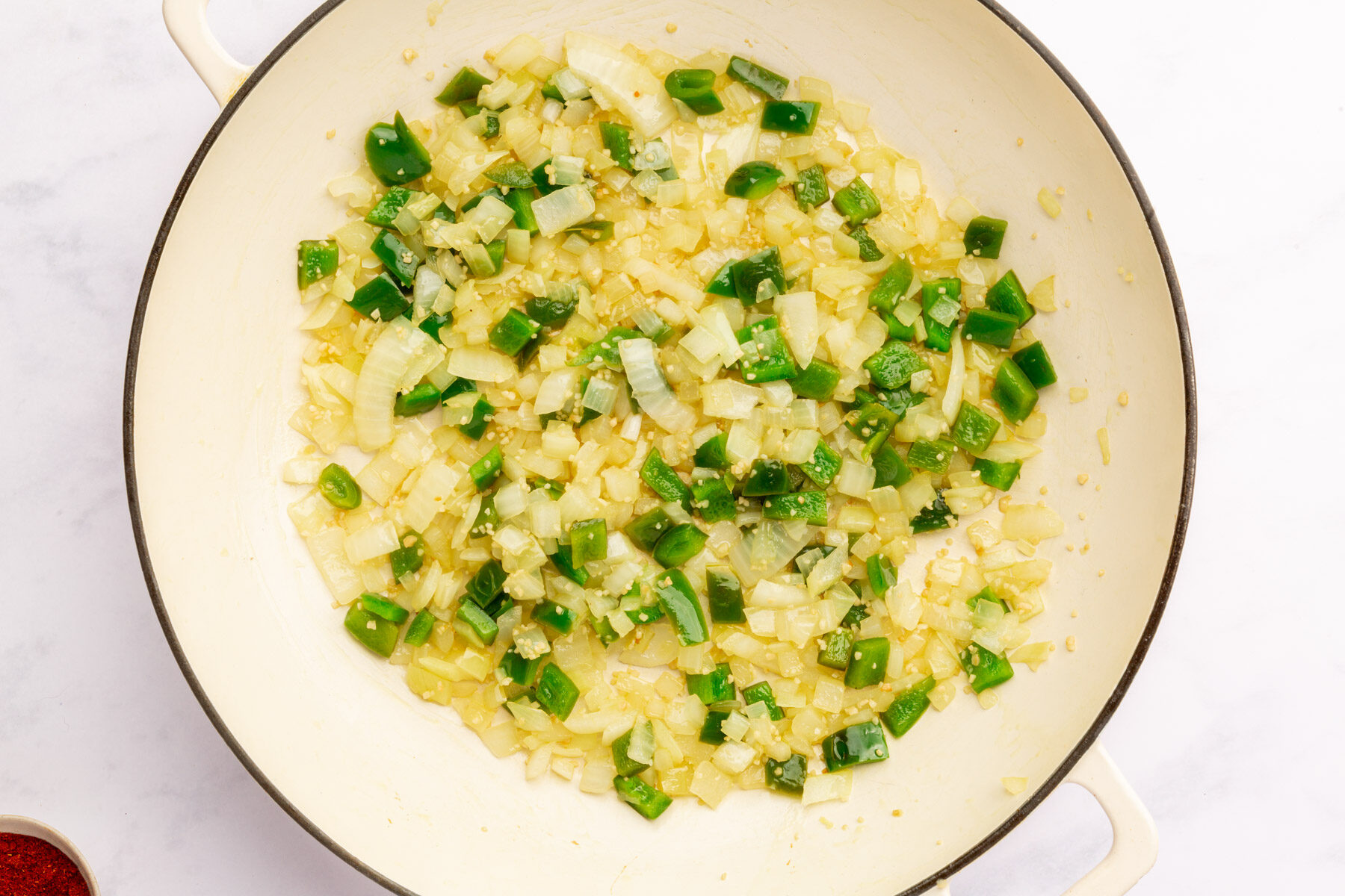 Large mixing bowl with minced garlic, olive oil, green bell pepper and yellow onion.