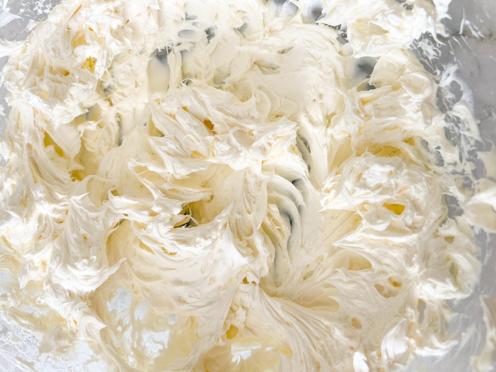 A close-up of whipped cream cheese in a glass mixing bowl, showing a fluffy and smooth texture.