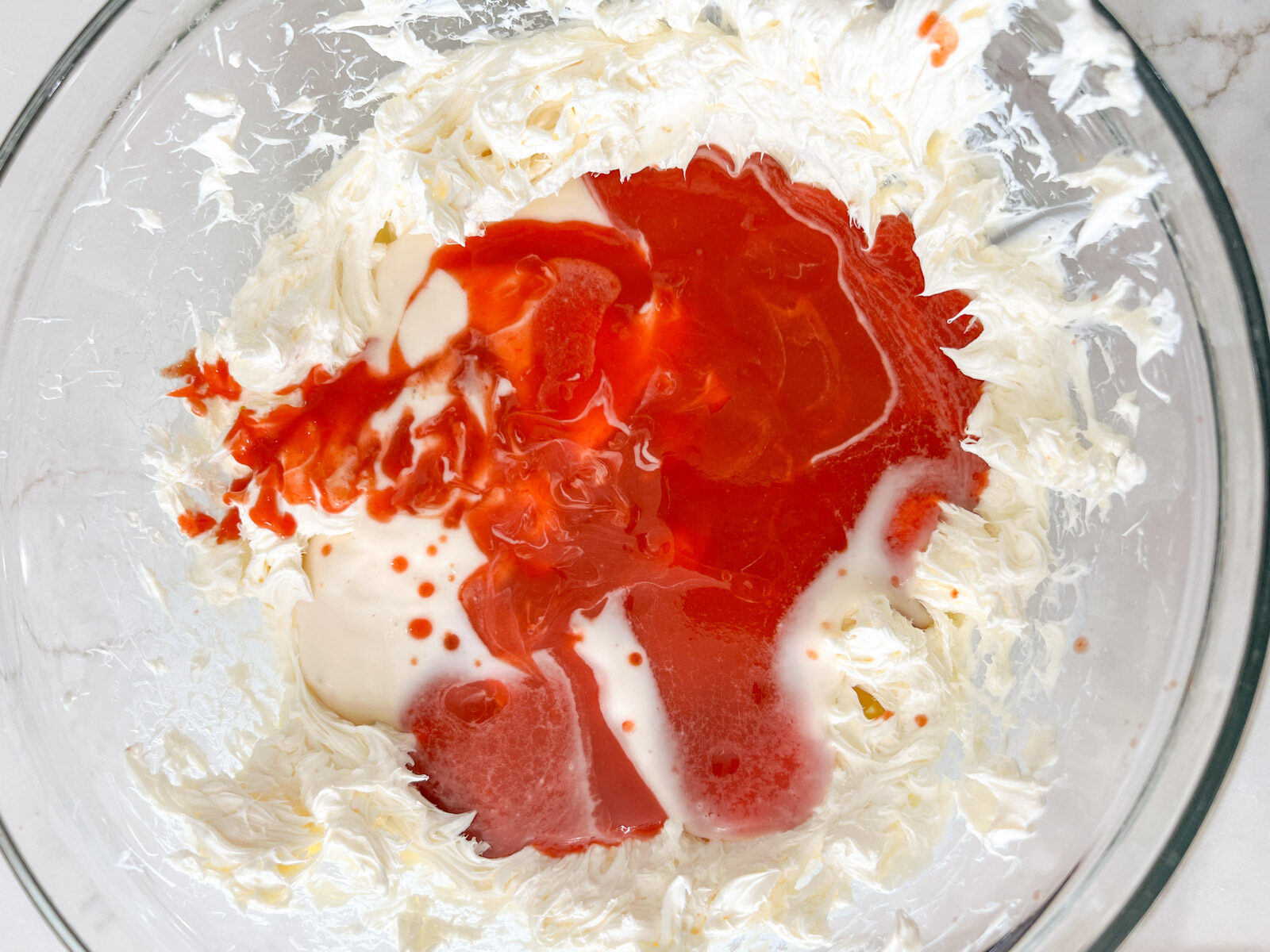 A glass bowl with whipped cream cheese, hot sauce, and ranch dressing before being mixed together.