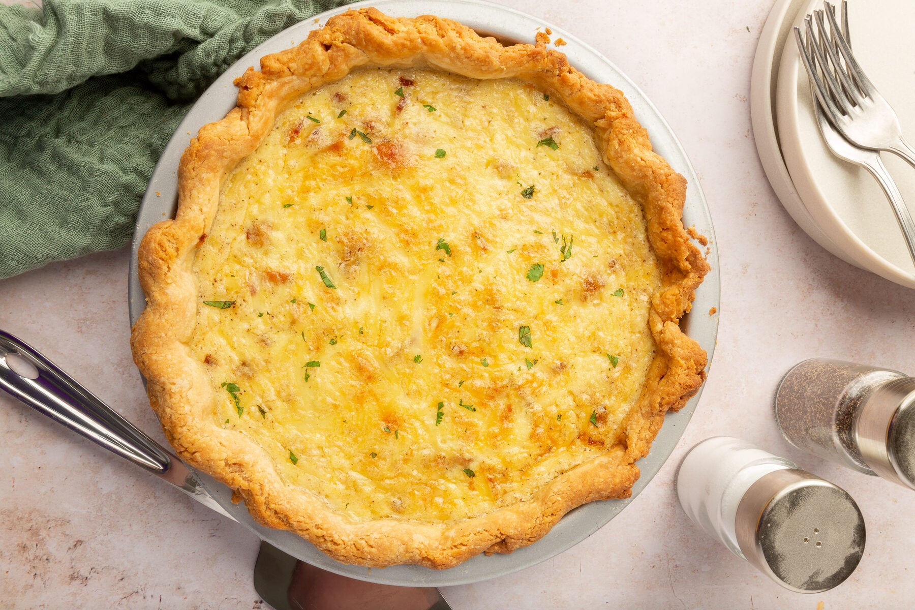 An overhead view of a fulled cooked gluten free quiche lorraine on a table with salt and pepper shakers off to the side.