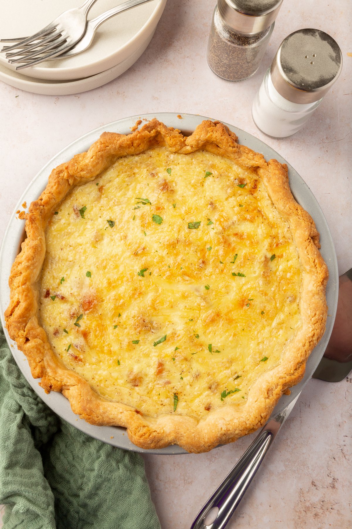An overhead view of a fulled cooked gluten free quiche lorraine on a table with salt and pepper shakers off to the side.