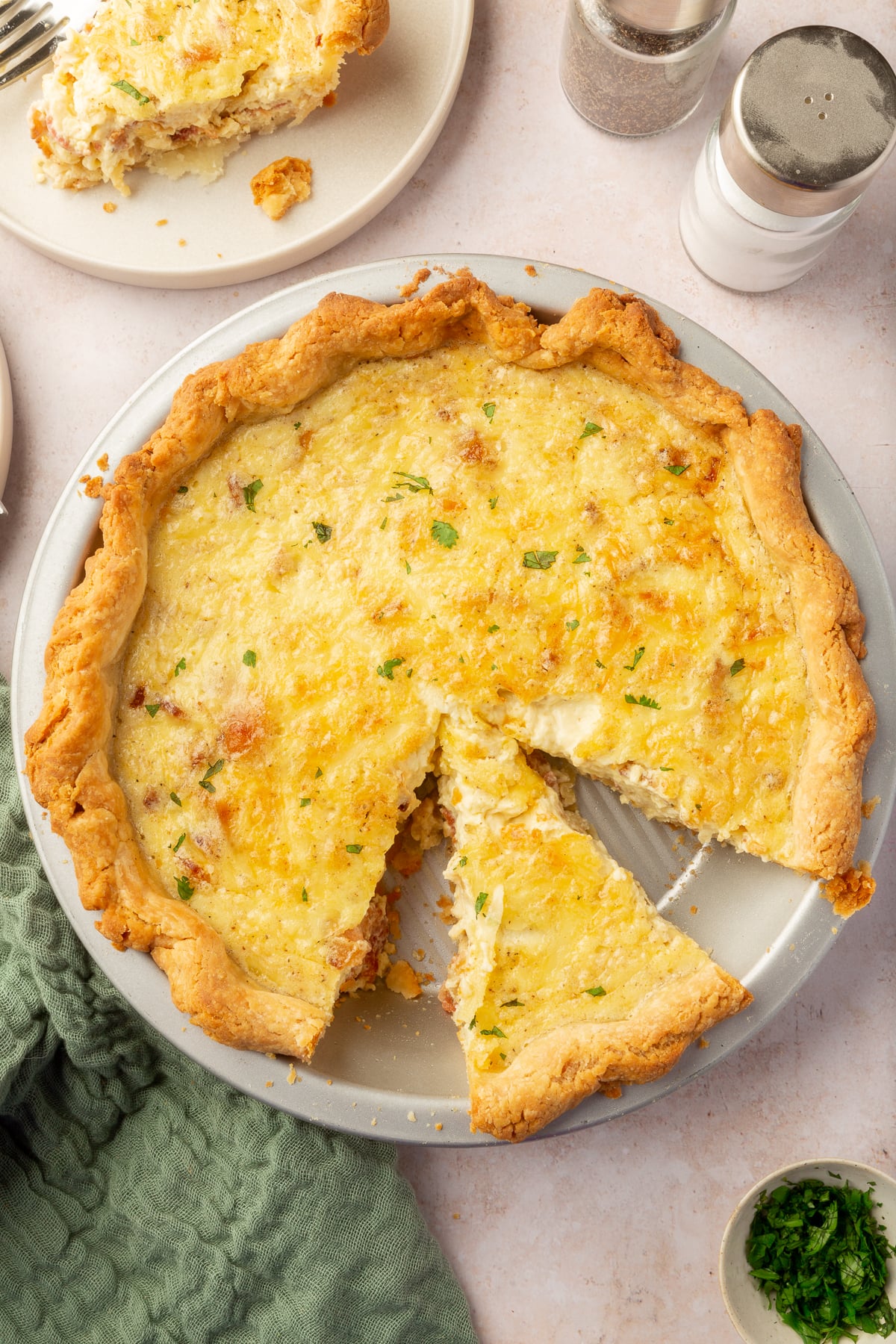 An overhead view of a partially sliced gluten-free quiche lorraine in a metal pie tin.