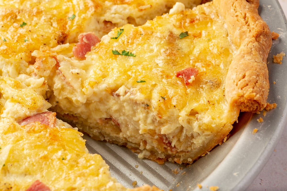 A partially sliced gluten-free quiche in a pie tin.