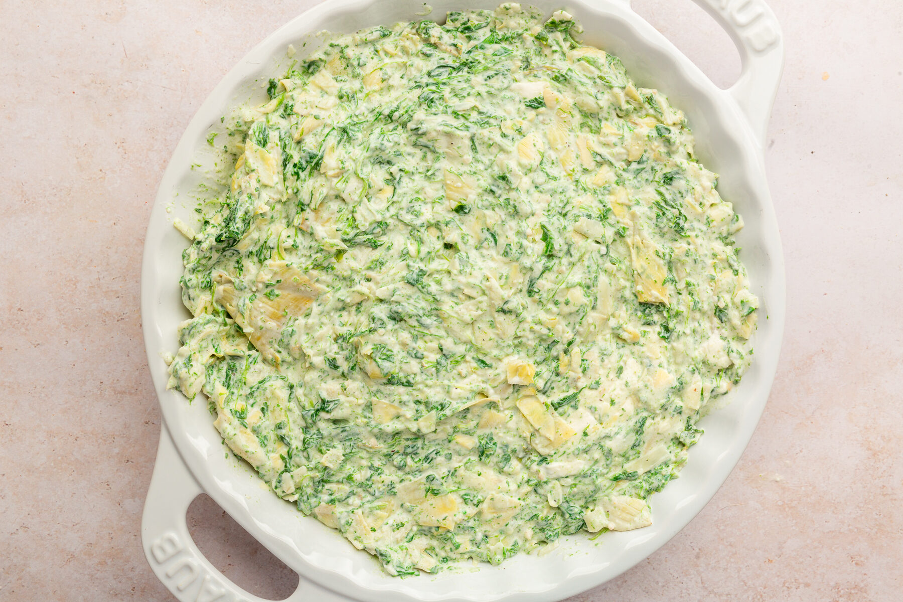 Image of spinach artichoke dip in white pie dish not yet baked.