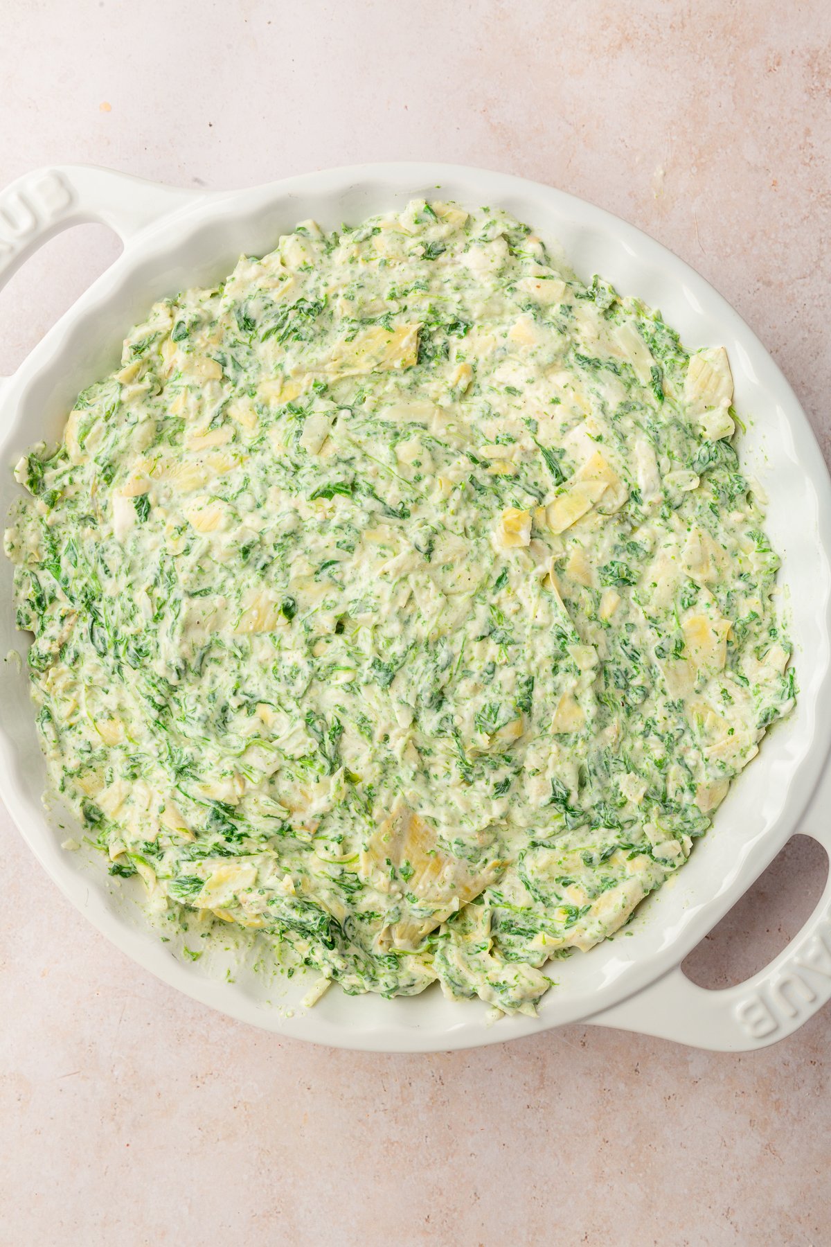 Image of spinach artichoke dip in white pie dish not yet baked.