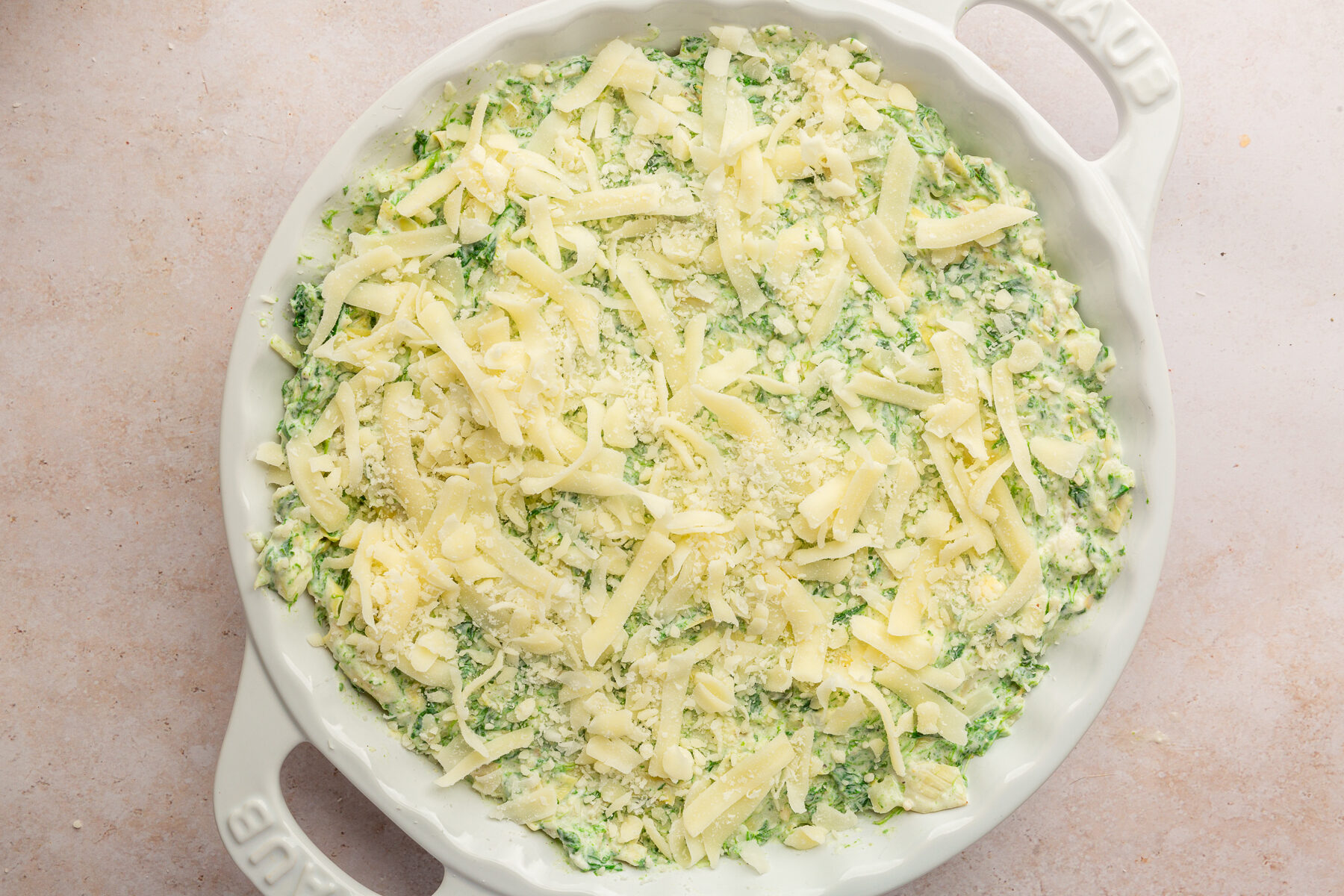 Image of spinach artichoke dip in white pie dish with mozzarella cheese on top, not yet baked.