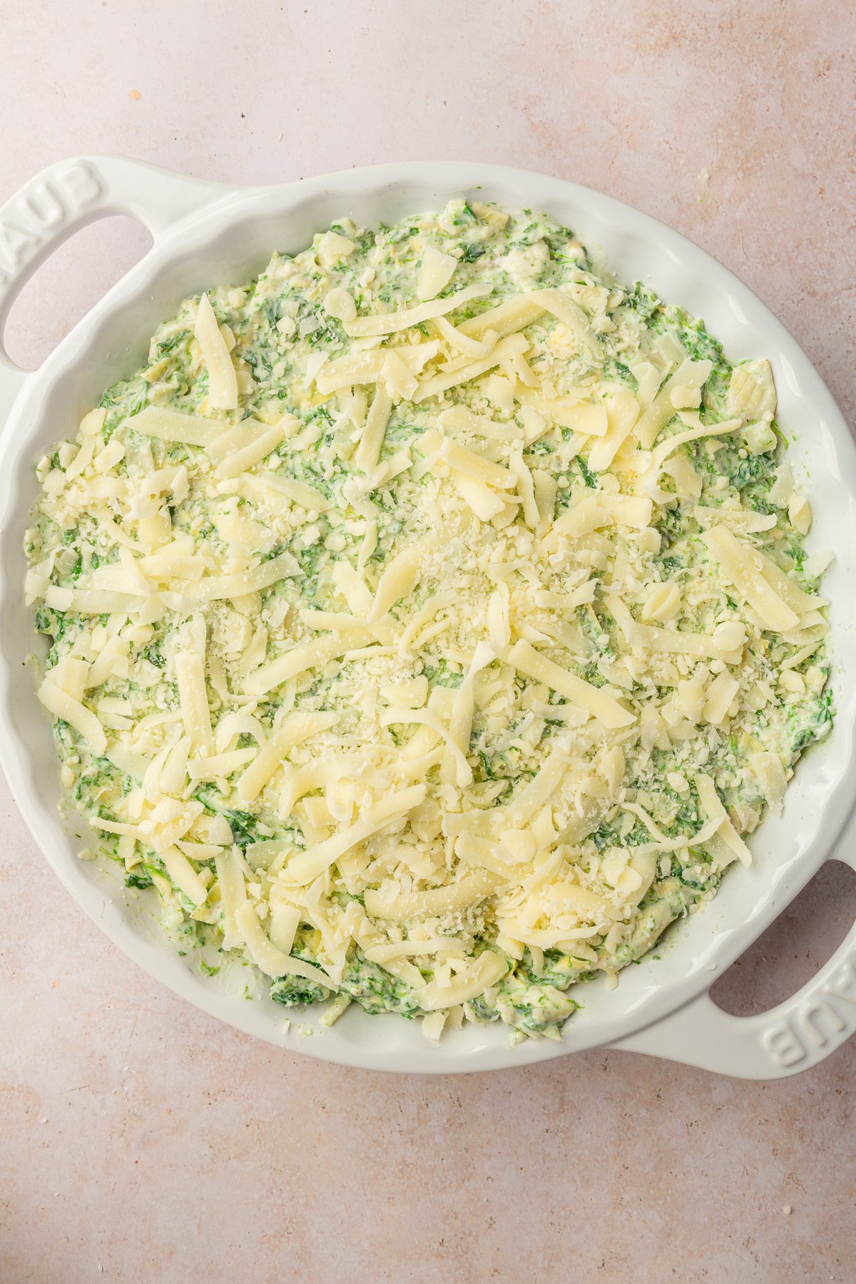 Image of spinach artichoke dip in white pie dish with mozzarella cheese on top, not yet baked.