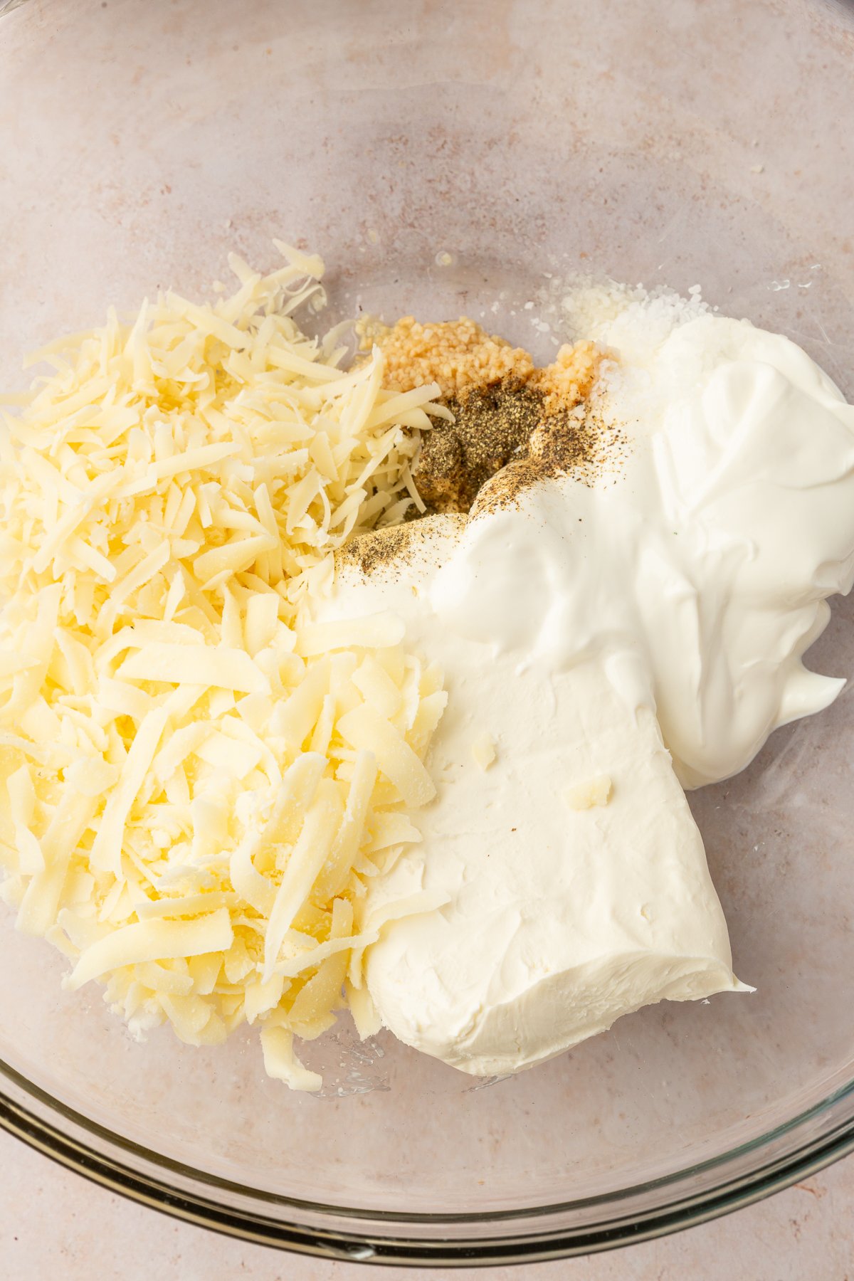 Sour cream, cream cheese, garlic, salt, pepper, Parmesan cheese and mozzarella cheese in a large, clear mixing bowl not yet mixed together.