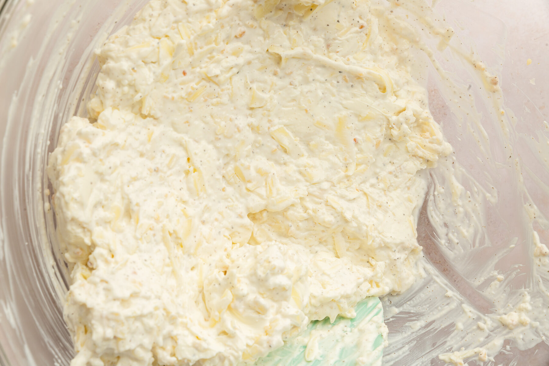 Sour cream, cream cheese, salt, pepper, garlic, Parmesan cheese, mozzarella cheese mixed together in a large, clear mixing bowl.