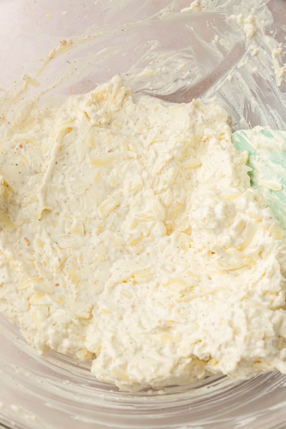 Sour cream, cream cheese, salt, pepper, garlic, Parmesan cheese, mozzarella cheese mixed together in a large, clear mixing bowl.