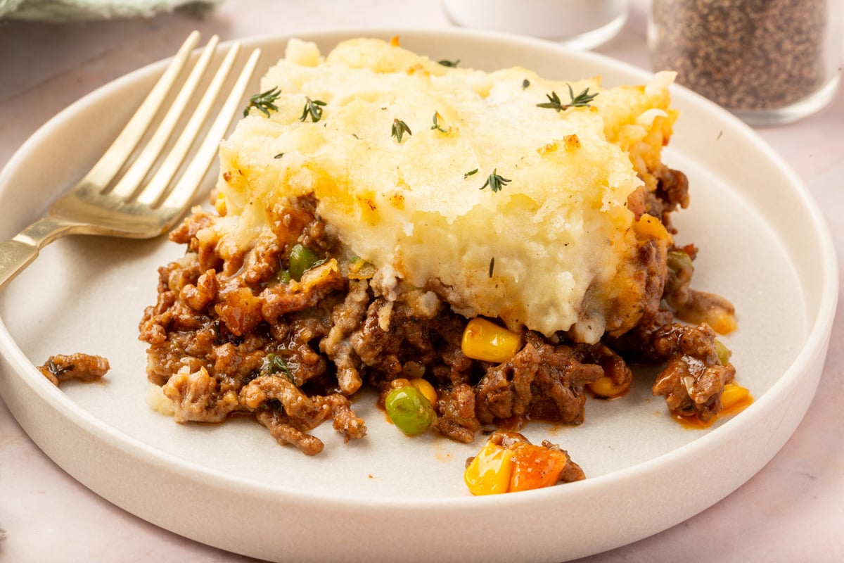 Close up image of a slice of gluten-free shepherd's pie on a white plate with a fork next to the slice of pie.