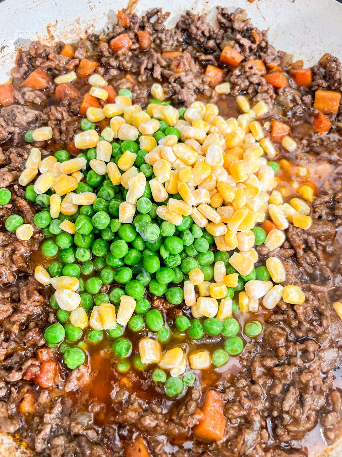 Frozen corn and peas being mixed into ground beef and carrot mixture