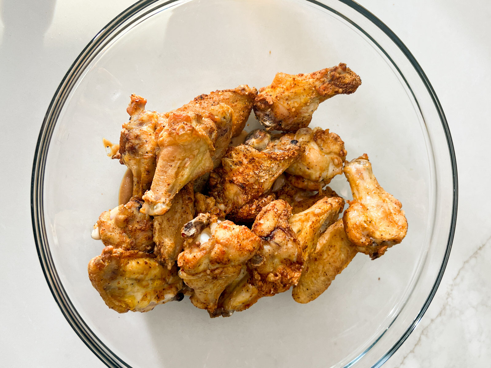 Baked chicken wings in a glass mixing bowl after cooking in the oven.