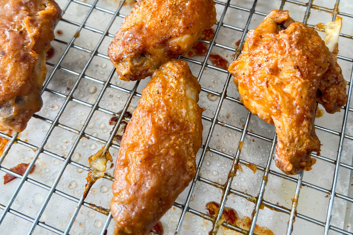 A close up of baked chicken wings tossed with peanut butter sauce on a wire rack topped baking sheet.