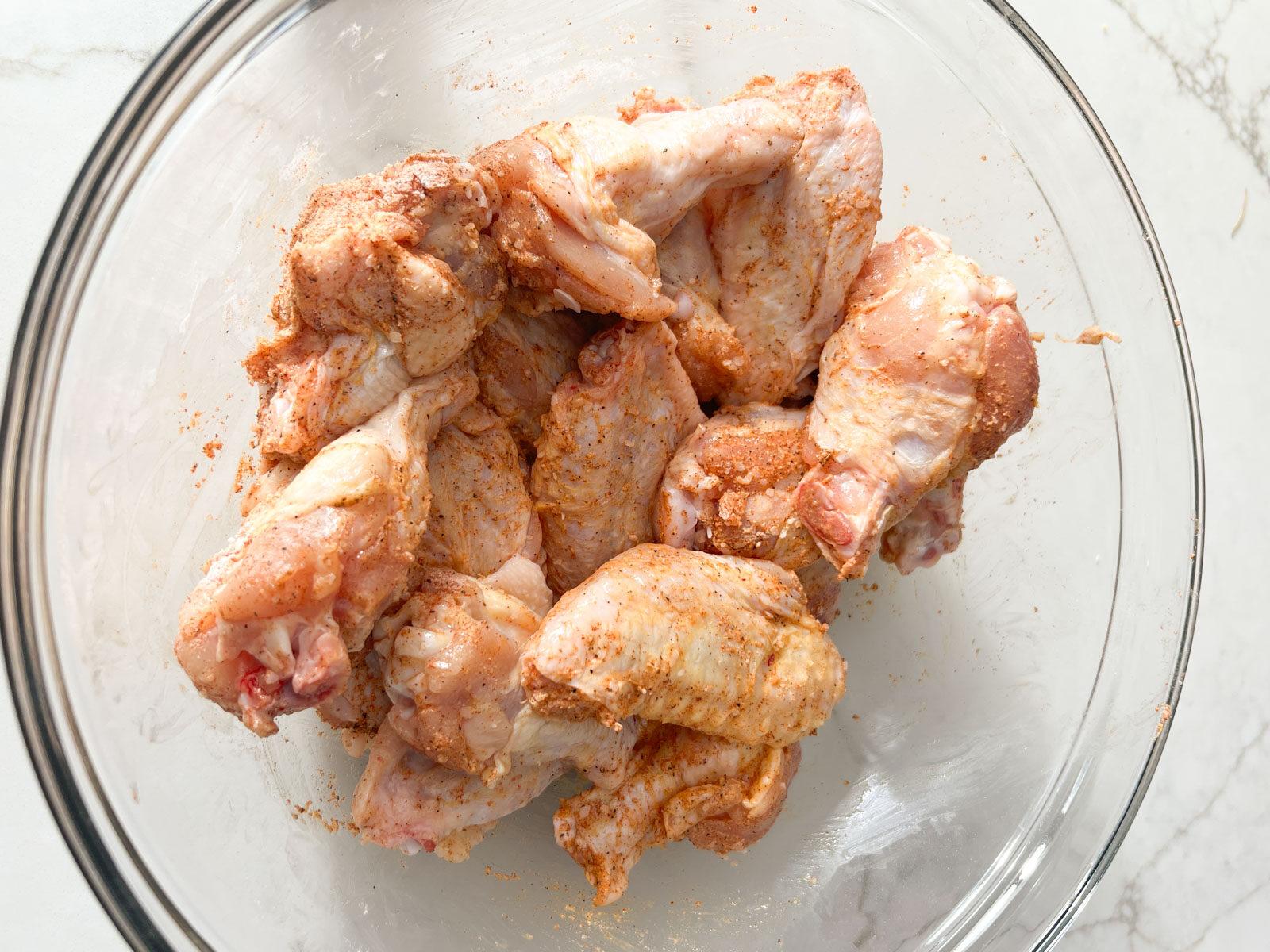 Raw chicken wings coated in baking powder and spices in a glass mixing bowl.