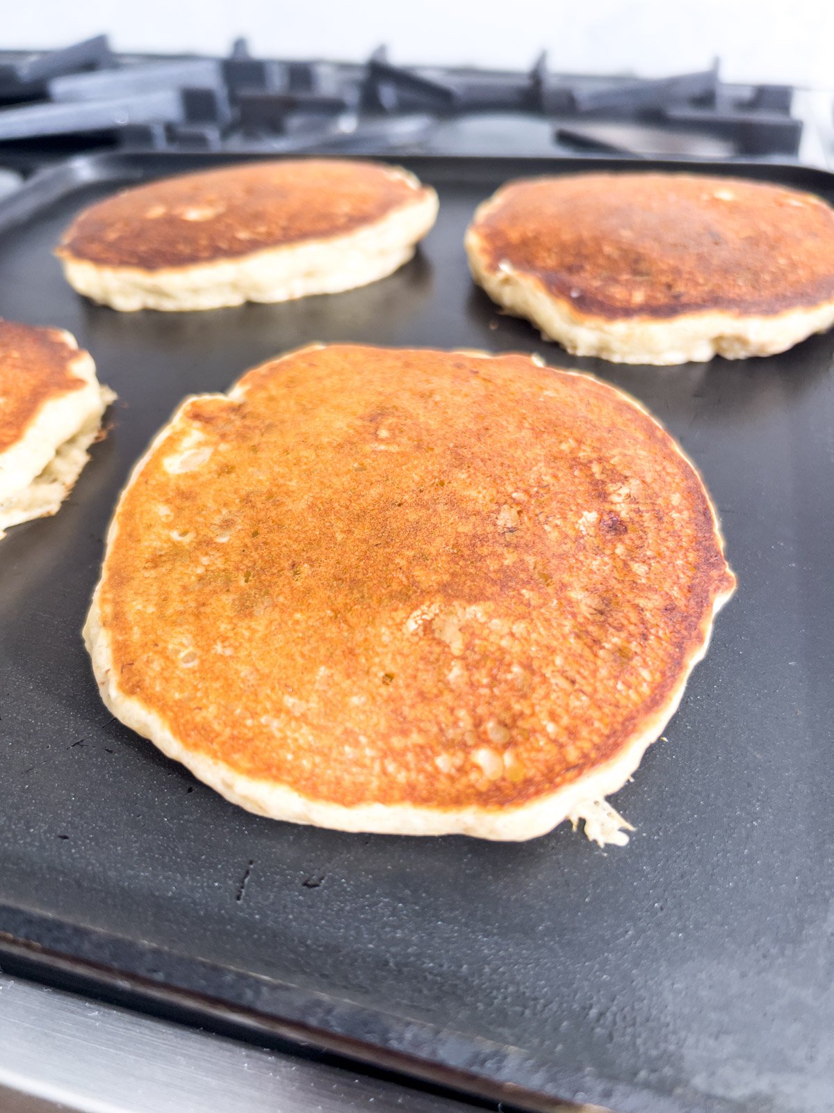 Golden-brown gluten-free banana pancakes on a griddle, with a crispy, caramelized top.