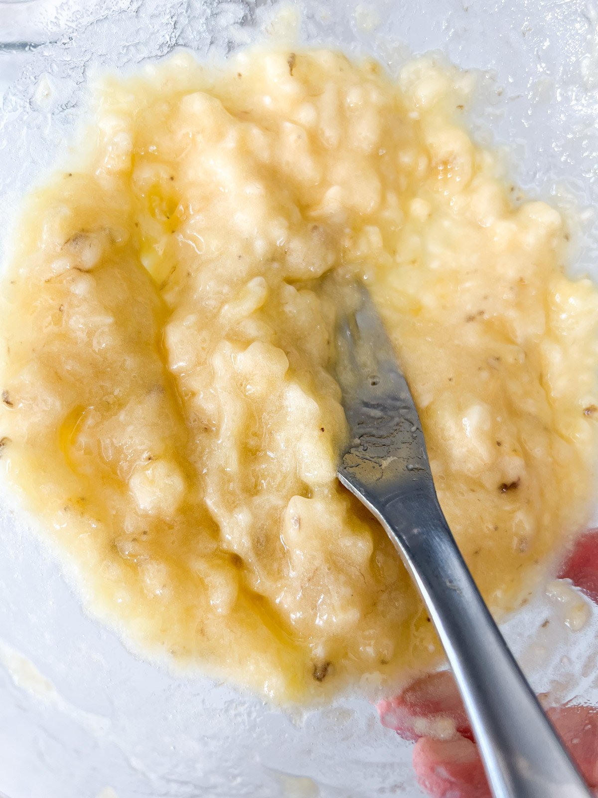 Mashed bananas in a glass bowl, with a fork blending them into a smooth mixture.