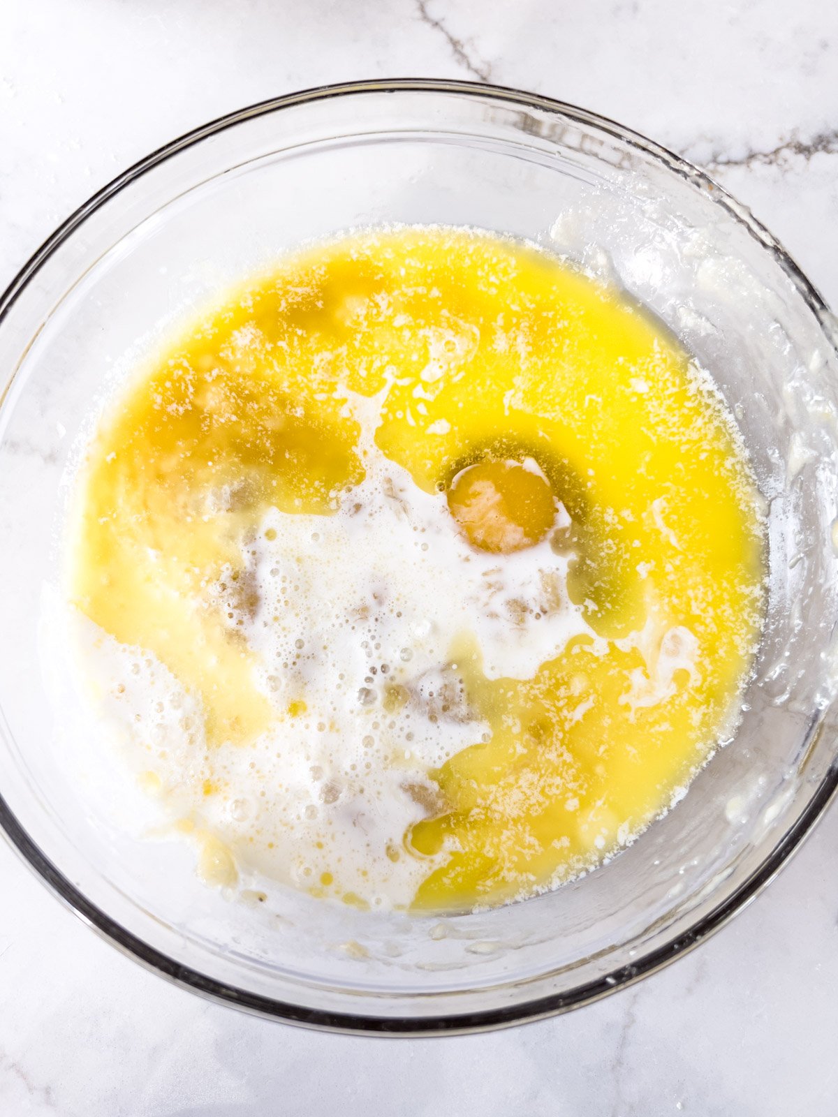 Wet ingredients, including mashed bananas, melted butter, milk, and egg, combined in a glass bowl.