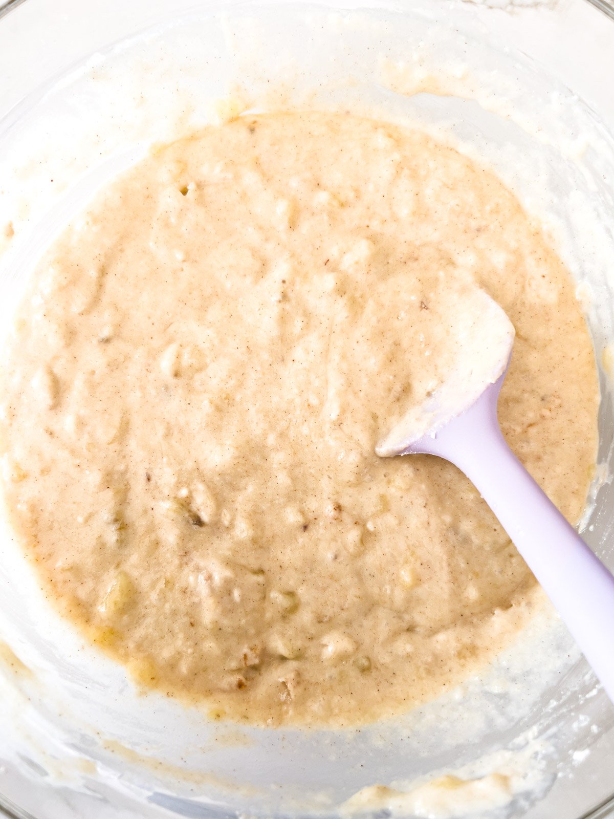Thick, creamy pancake batter in a glass bowl, with visible banana pieces mixed in.