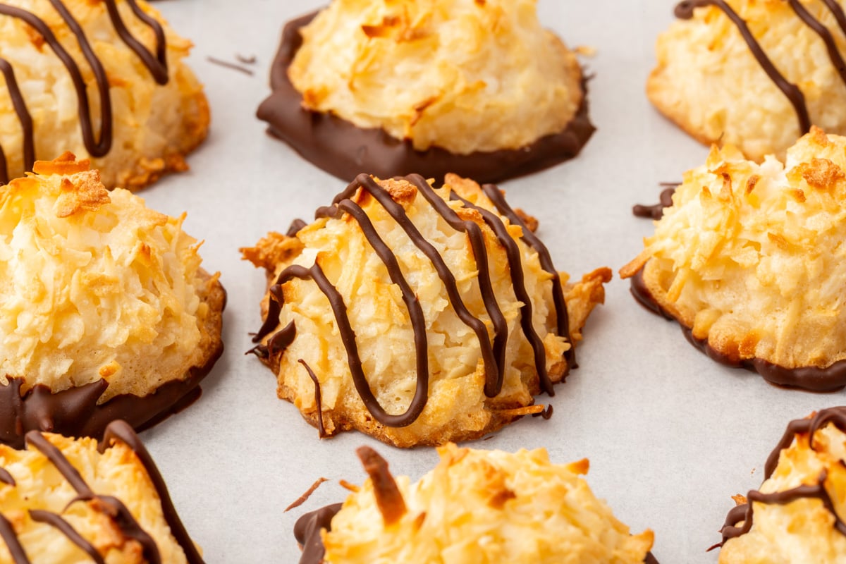 Overhead view of multiple coconut macaroons arranged on parchment paper, featuring a mix of chocolate-dipped and chocolate-drizzled finishes.