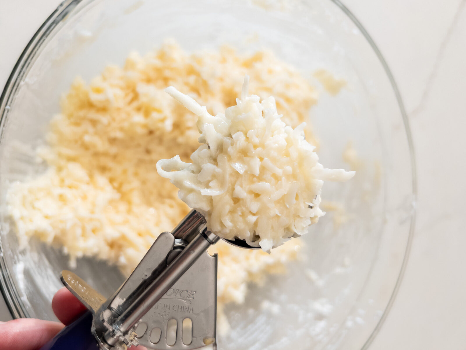 Cookie scoop lifting a rounded portion of coconut macaroon batter.