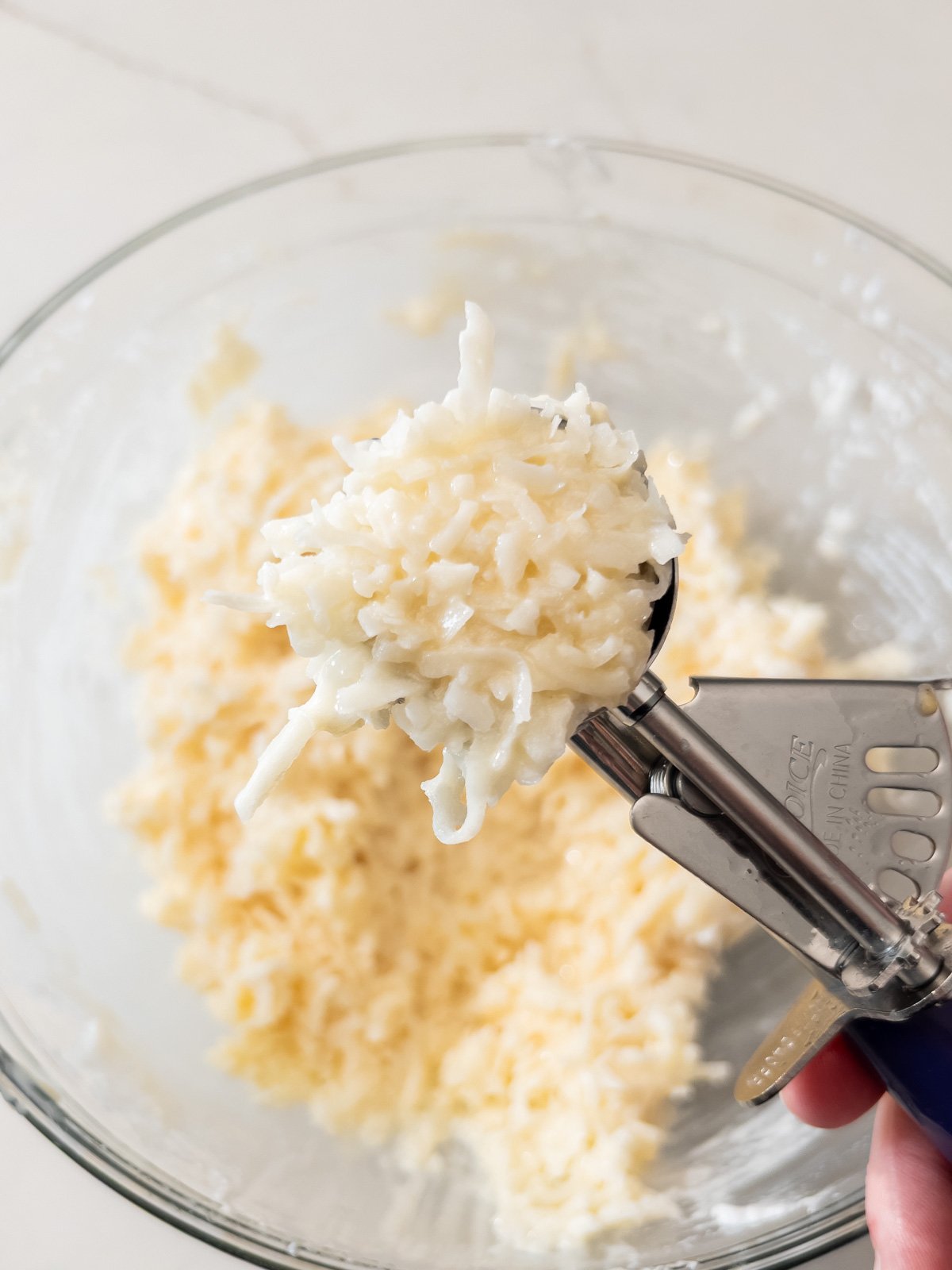 Cookie scoop lifting a rounded portion of coconut macaroon batter.