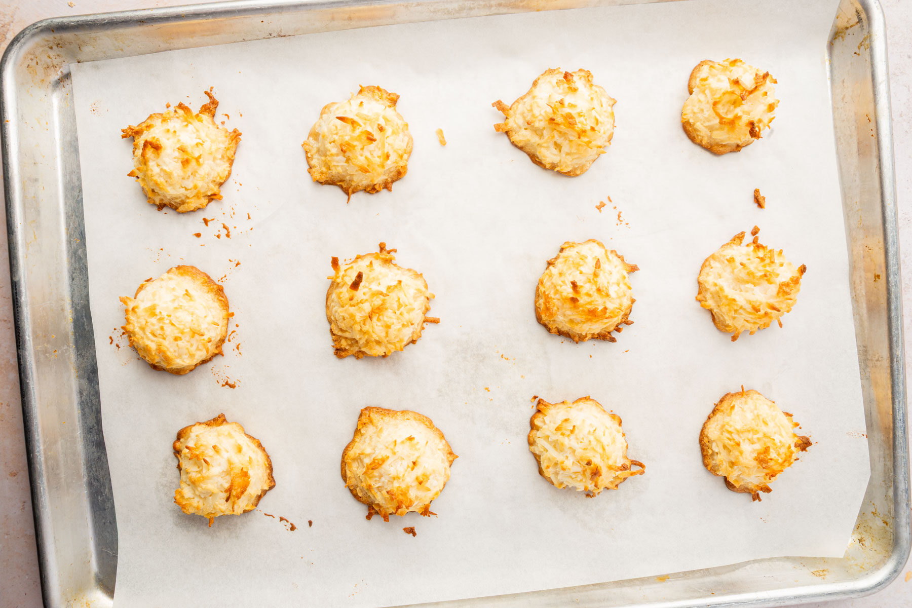 Baked coconut macaroons with golden-brown edges cooling on a parchment-lined baking sheet.