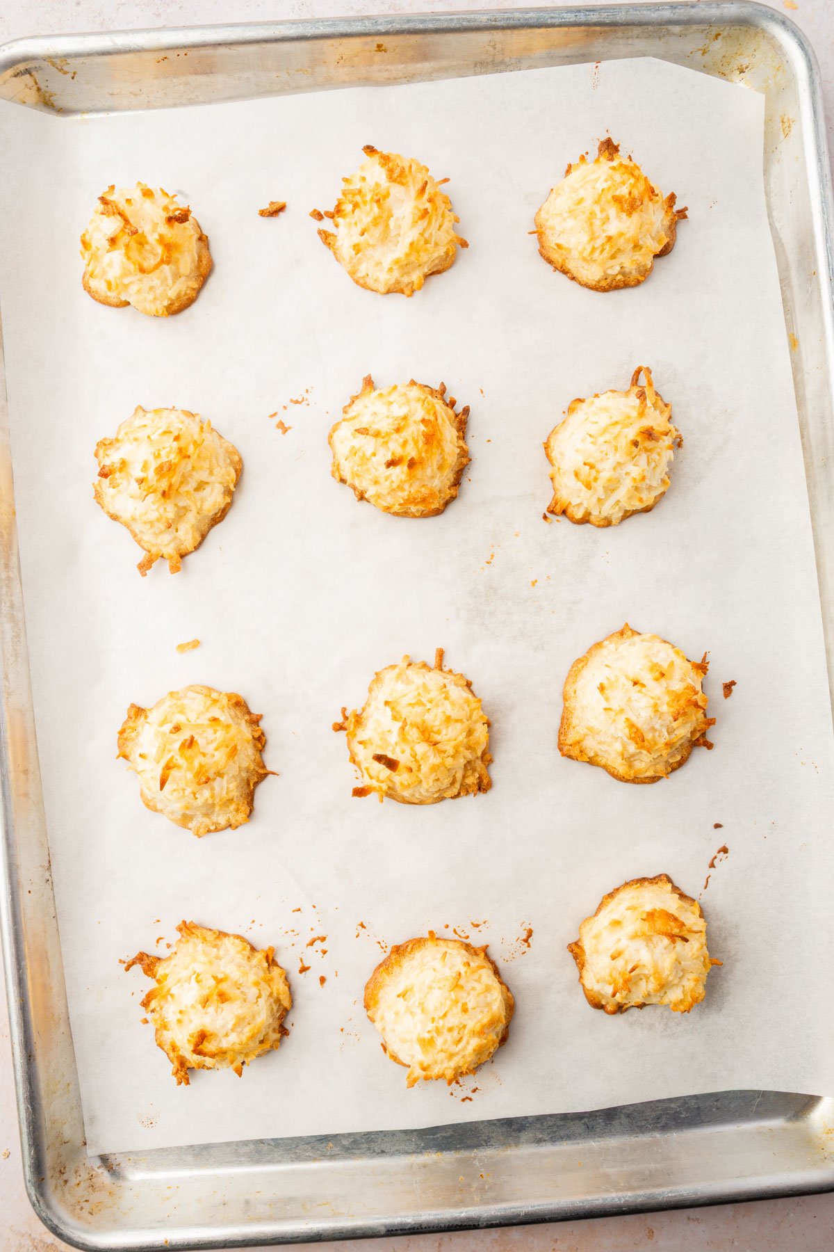 Baked coconut macaroons with golden-brown edges cooling on a parchment-lined baking sheet.